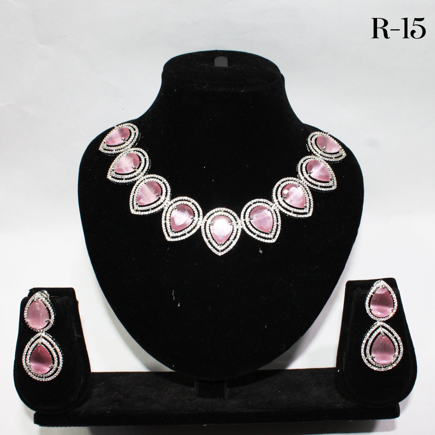 Jewelry set with pink gemstones on a black stand against a white background