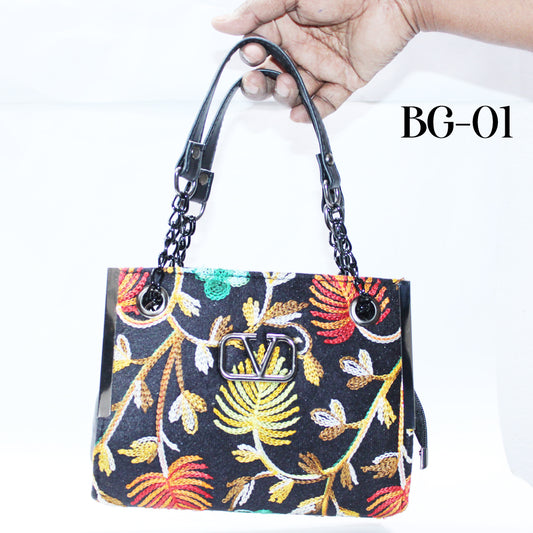 Handbag with floral pattern and visible brand logo held by a hand against a white background.